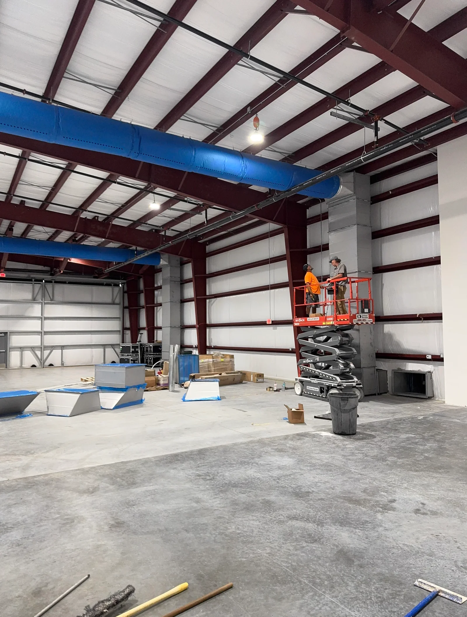 Blue HVAC ductwork installed across steel beam structure in commercial warehouse with polycarbonate roof panels