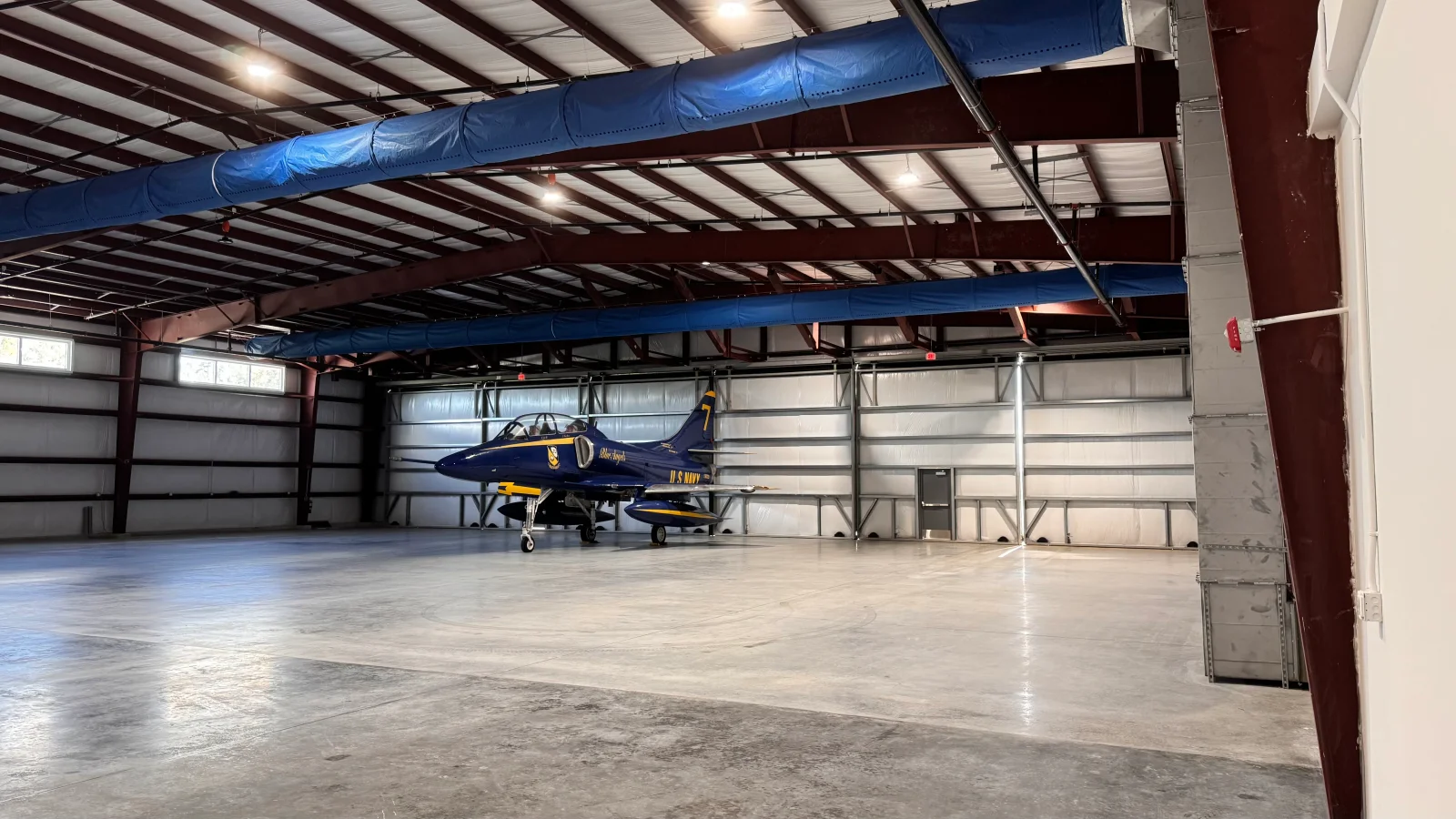 Blue-wrapped HVAC ductwork installed across hangar ceiling with steel beams and concrete floor