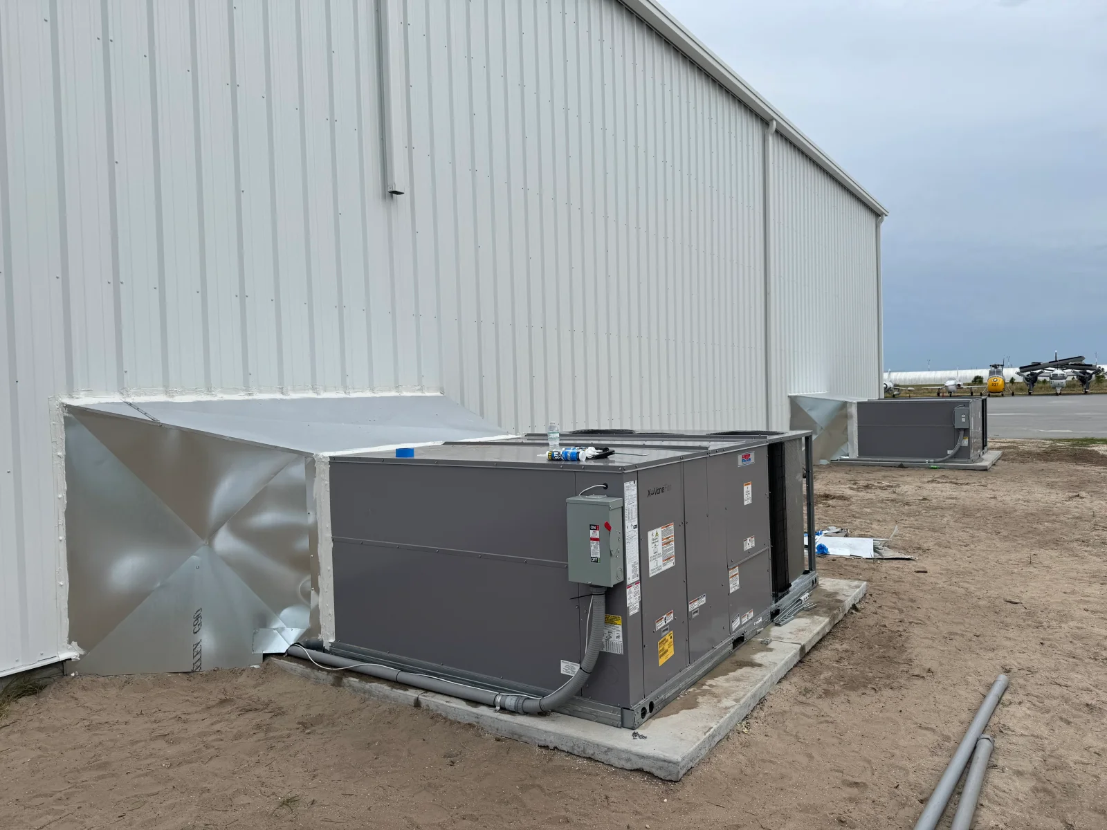 Commercial rooftop HVAC unit installation with metal building and concrete pad foundation